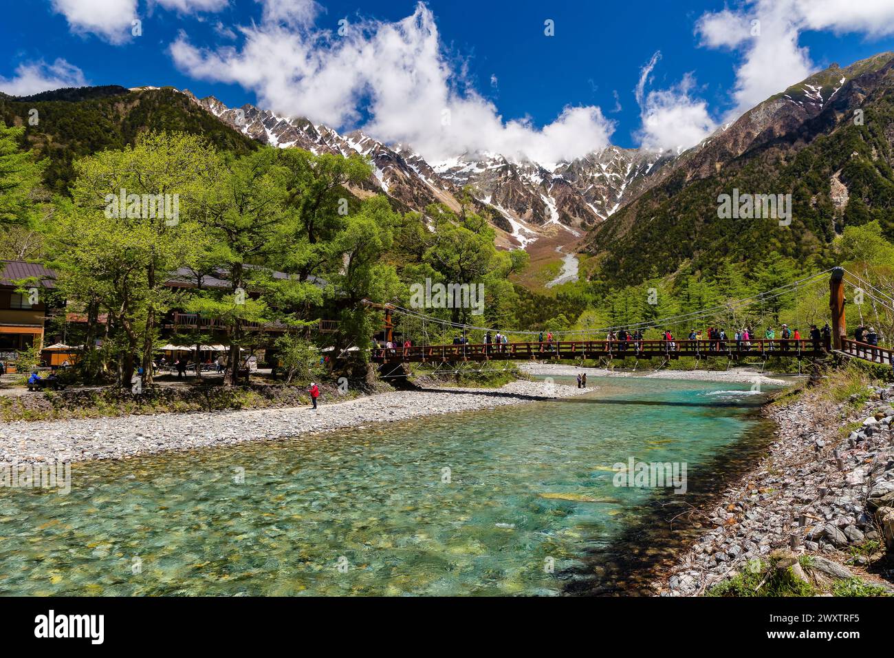 KAMIKOCHI, JAPAN - 24. MAI 2023: Wanderer und Touristen auf Kappabashi mit den schneebedeckten Gipfeln des Kotaka-Gebirges dahinter. Kamikochi, Präfektur Nagano Stockfoto