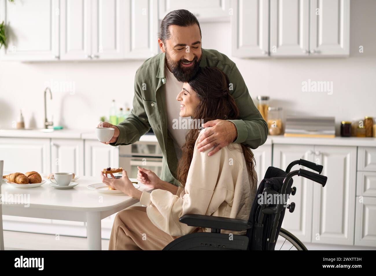 Freudige attraktive Frau mit Behinderung im Rollstuhl, die mit ihrem liebevollen Ehemann frühstückt Stockfoto