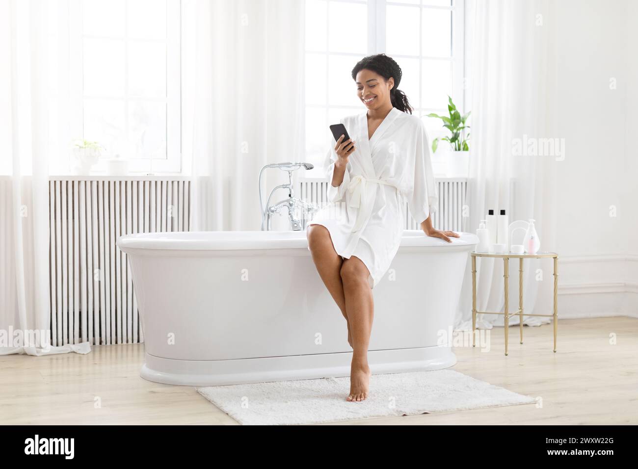 Frau im Bademantel, die das Telefon in der Badewanne benutzt Stockfoto