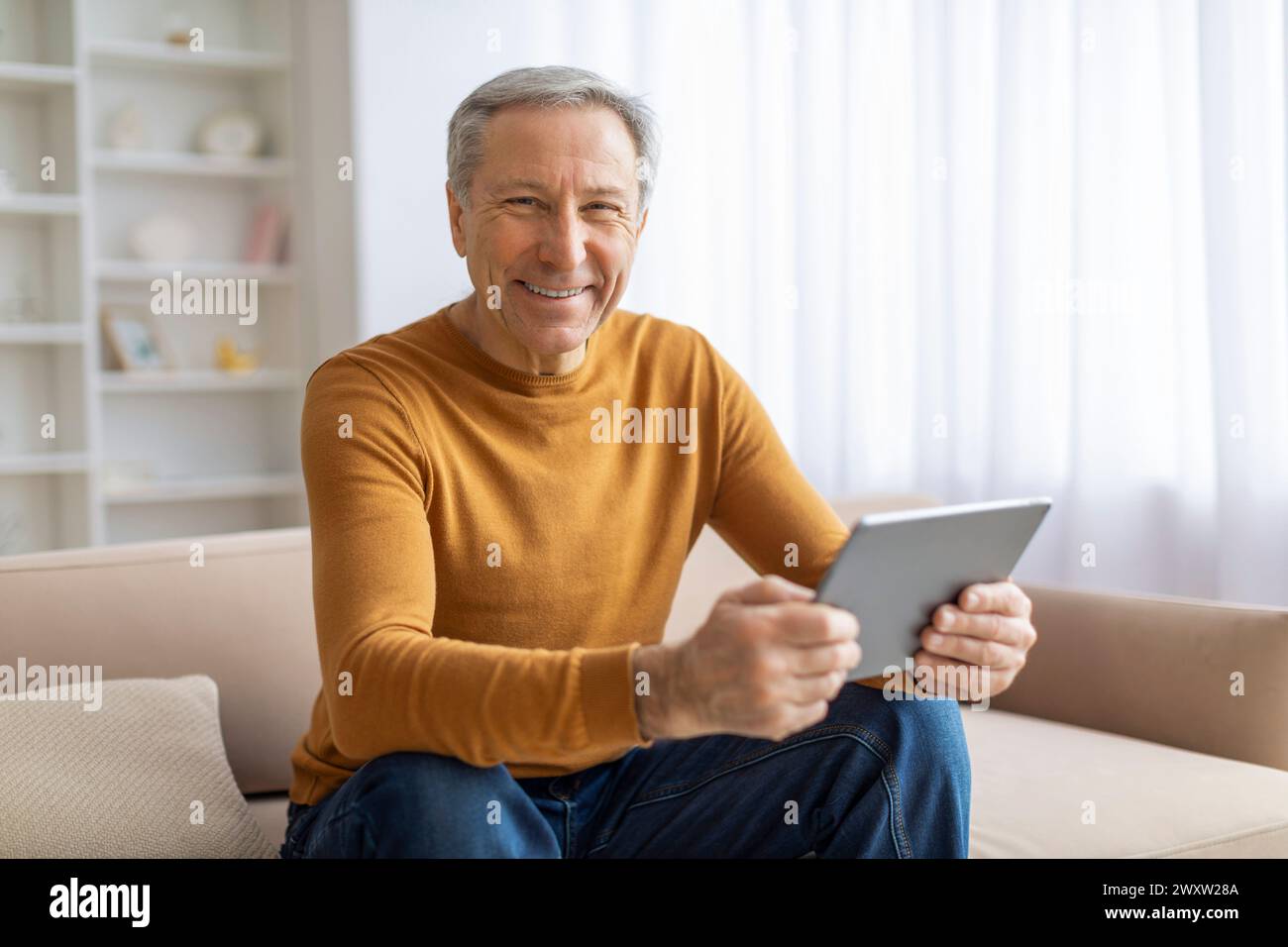 Glücklicher älterer Mann, der zu Hause ein Tablet benutzt Stockfoto