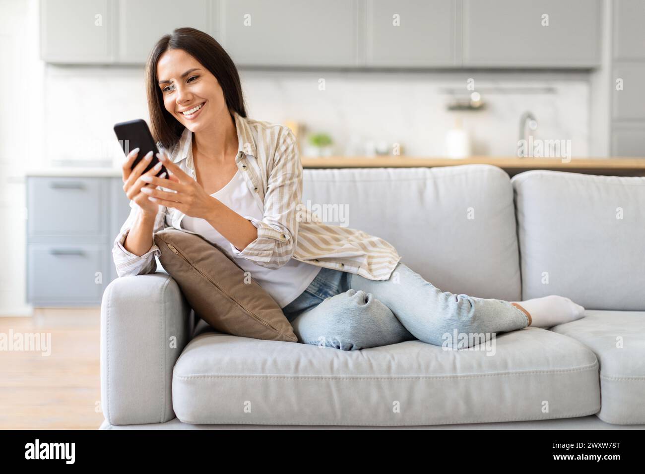 Glückliche Frau, die zu Hause auf der Couch ihr Handy durchsucht Stockfoto