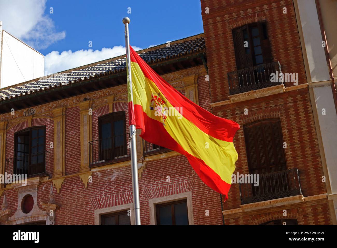 Spanische Nationalflagge, die vor dem traditionellen Backsteingebäude Malaga hisst Stockfoto