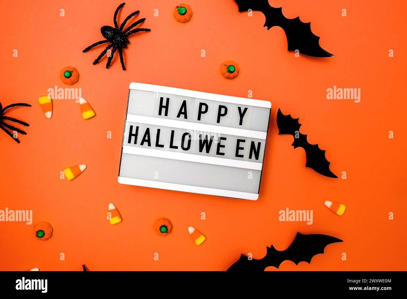Traditionelles Halloween-Dekor und Süßigkeiten auf orangem Hintergrund mit Happy Halloween auf dem Leuchtkasten Stockfoto