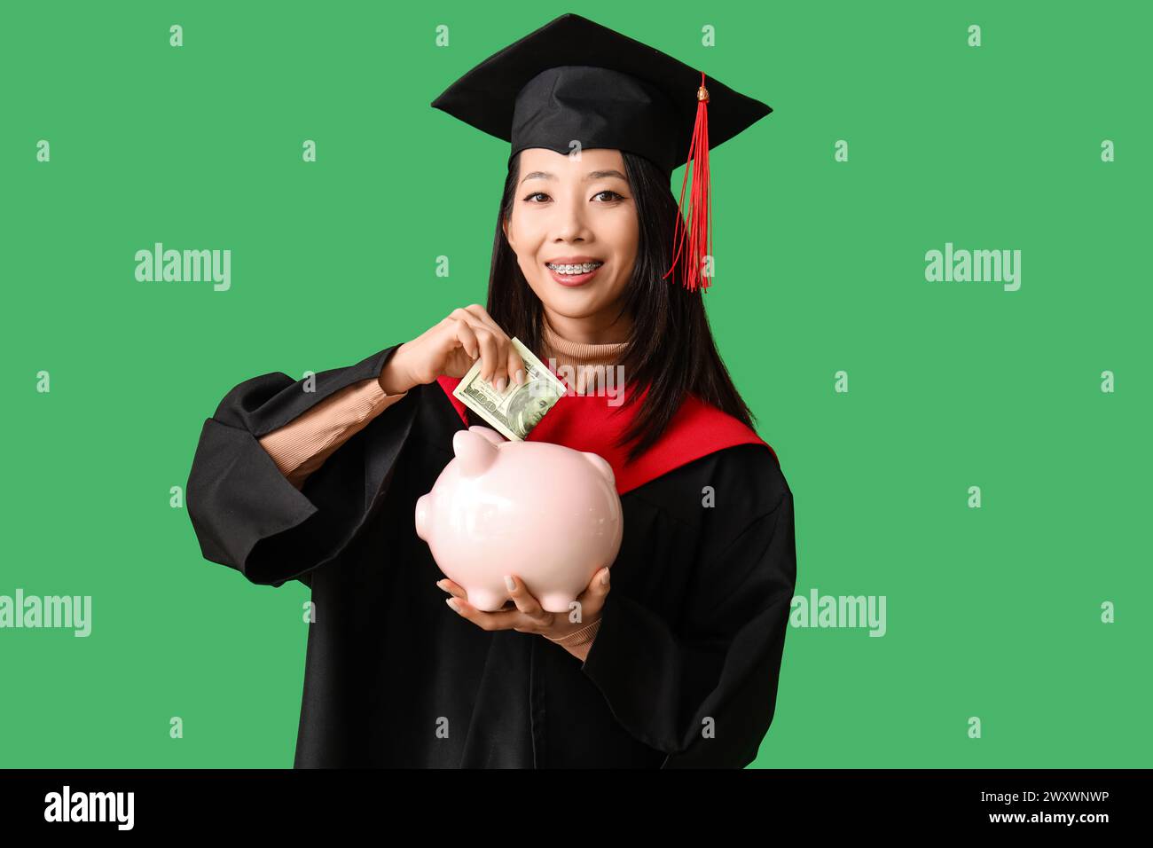 Asiatische Studentin, die Geld in Sparschweine auf grünem Hintergrund investiert. Studiengebühren-Konzept Stockfoto