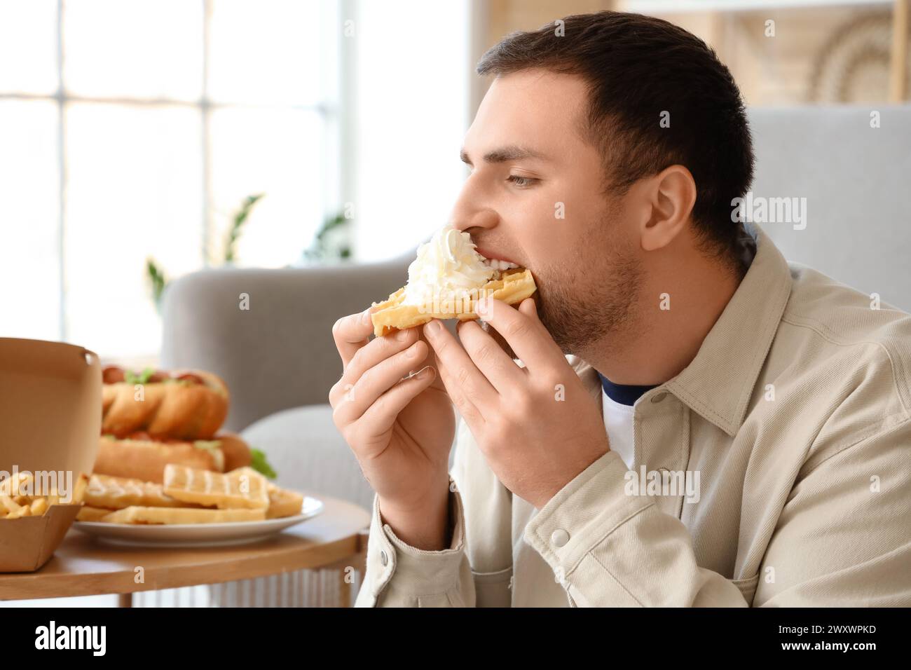 Junger Mann, der zu Hause Waffeln isst, Nahaufnahme. Das Konzept des Überessens Stockfoto