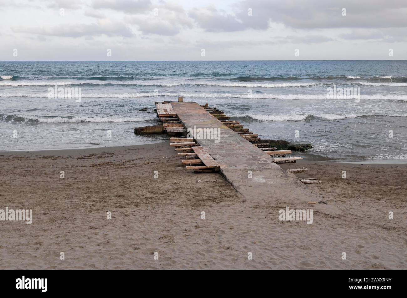 Holzsteg führt unter bewölktem Himmel an einem Sandstrand in das bewegte Meer, Diana Marina, Ligurien, Italien Stockfoto