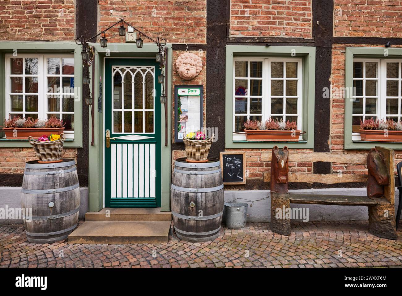 Eingangsbereich eines Restaurants in einem historischen Fachwerkhaus mit Eingangstür, weißen Fenstern, historischen Holzfässern und Blumenkörben Stockfoto