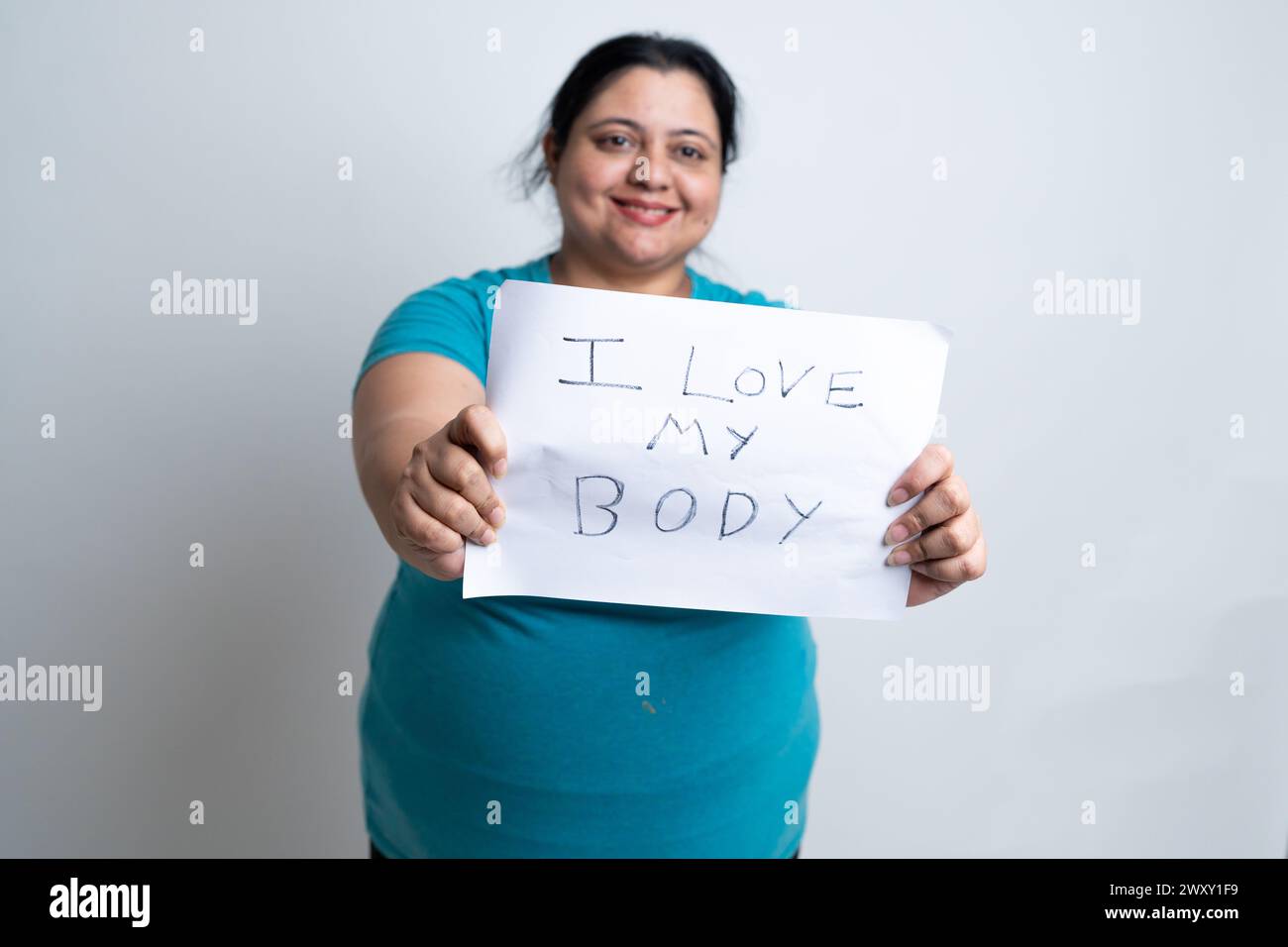 Übergewichtige, fette indische Frau, die weißes Papier hält, geschrieben: "ich liebe meinen Körper." Isoliert über weißem Hintergrund. Plus-Größe weiblich. Selbstliebe-Konzept. Stockfoto