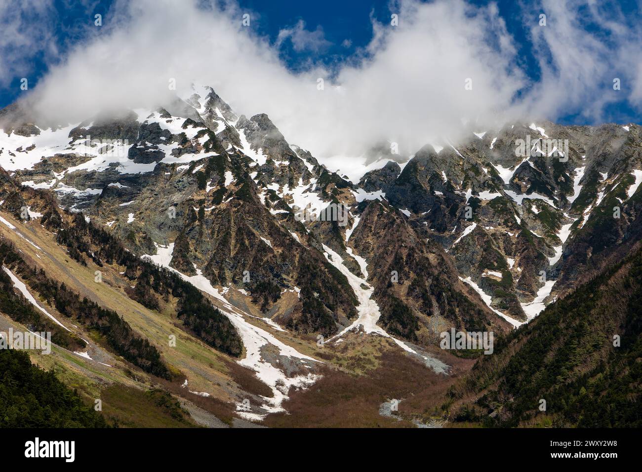 Wolken über dem Gipfel hoher, zerklüfteter, schneebedeckter Berggipfel Stockfoto