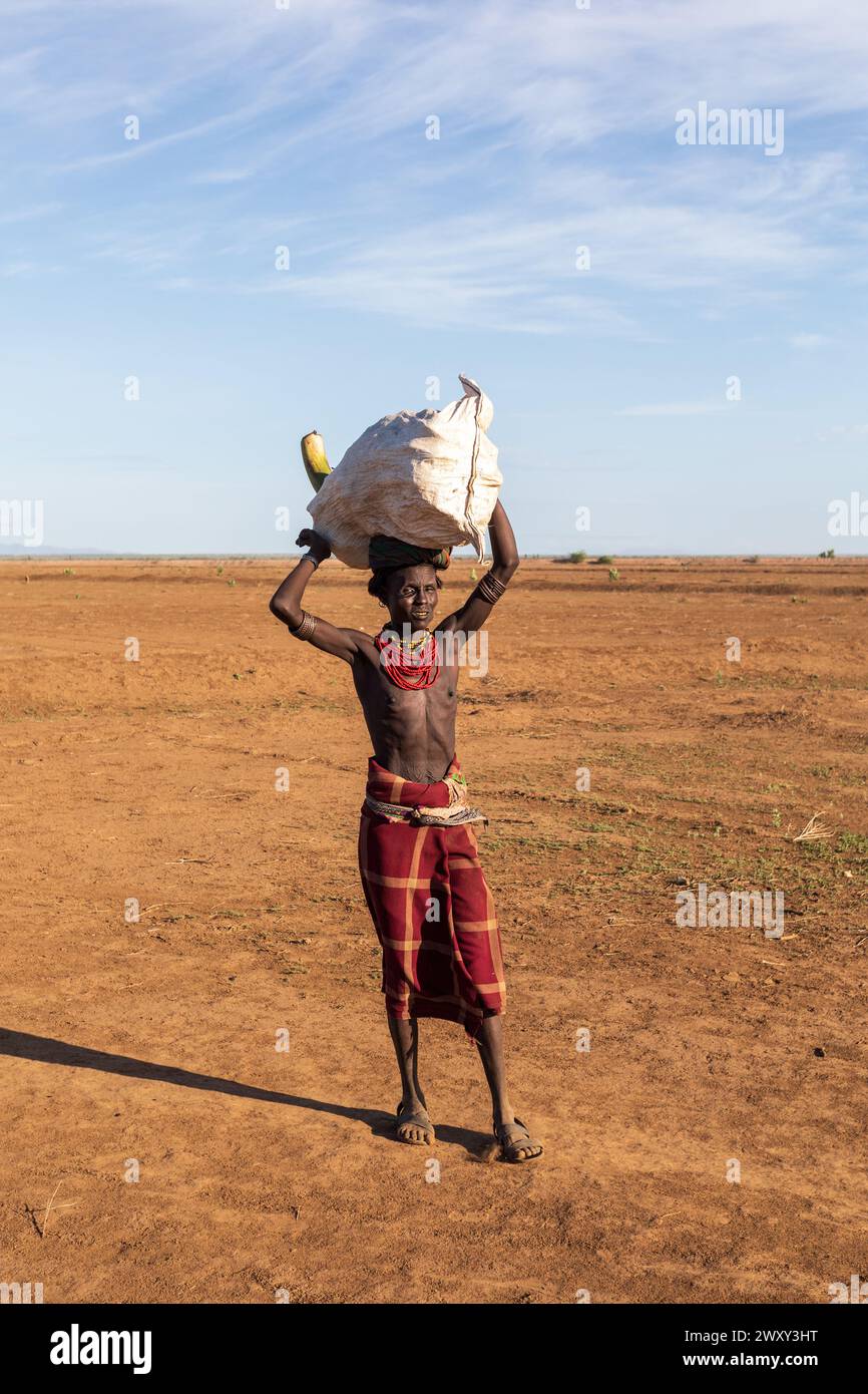 Omorate, Omo Valley, Äthiopien - 11. Mai 2019: Ein Mann aus dem afrikanischen Stamm Dasanesh trägt eine Tasche auf dem Kopf. Daasanach sind die Bewohner der kushitischen ethnischen Gruppe Stockfoto