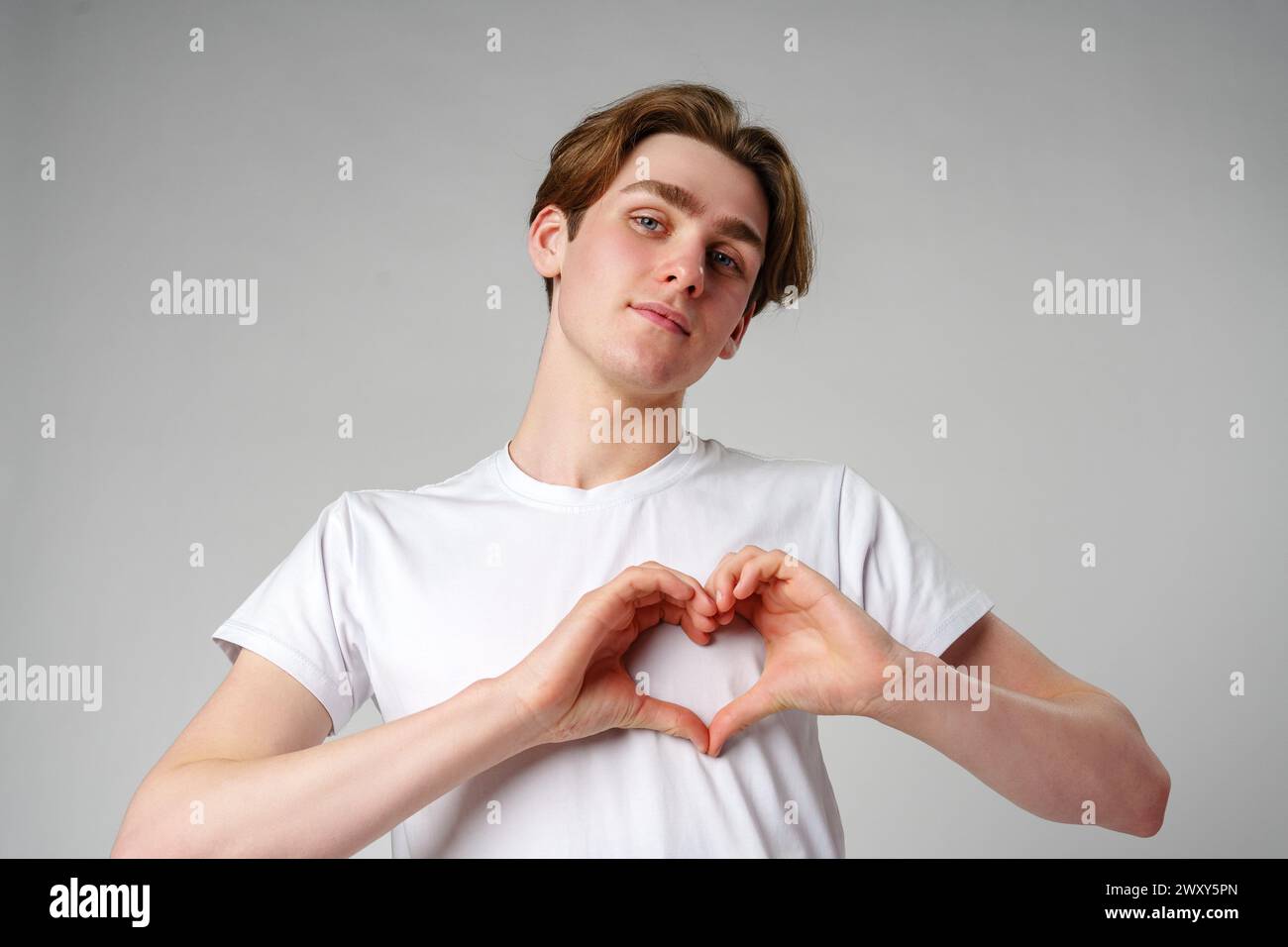 Junger Mann, der Herzform macht, mit Händen vor einem schlichten Hintergrund Stockfoto