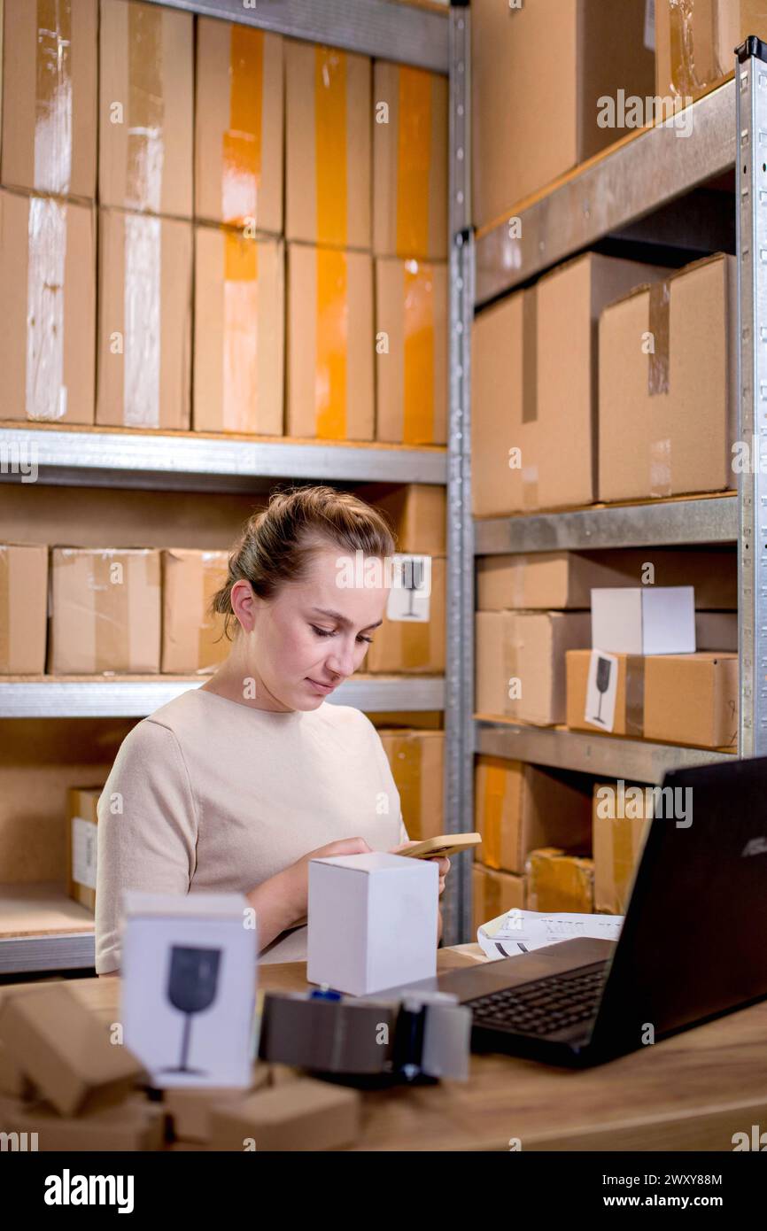 Junge Unternehmer Kleinunternehmen, die Internetbestellungen auf dem Smartphone überprüfen und verpackte Artikel für die Lieferung an Kunden vorbereiten. Stockfoto