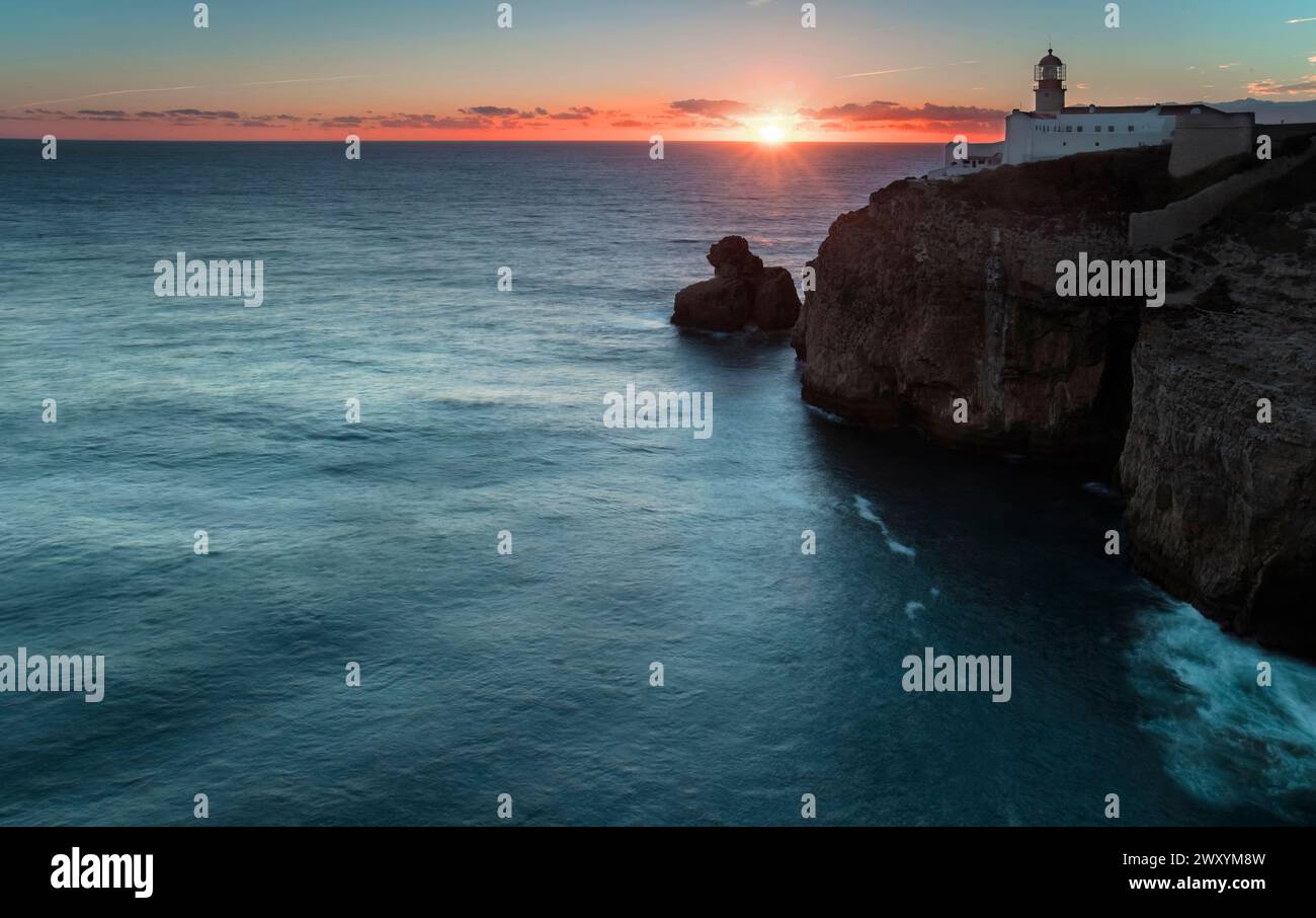 Ein ruhiger Sonnenaufgang mit warmen Farbtönen hinter der Cape St. Vincent Lighthouse thront auf zerklüfteten Klippen mit Blick auf den ruhigen Atlantik. Stockfoto
