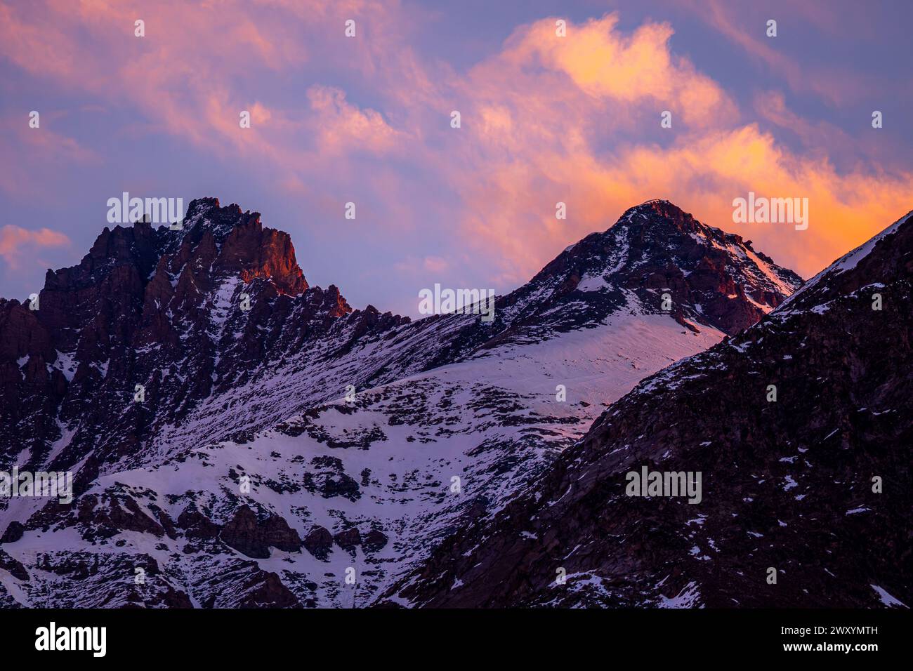 Die Dämmerung steigt auf die Berge mit einem atemberaubenden alpenglow hinab und beleuchtet die schneebedeckten Gipfel vor einem Zuckerwattenhimmel Stockfoto