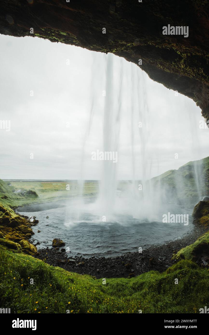 Grüne isländische Landschaft mit einem herrlichen Wasserfall, der hinabstürzt und einen einzigartigen Blick hinter dem Wasservorhang bietet. Stockfoto