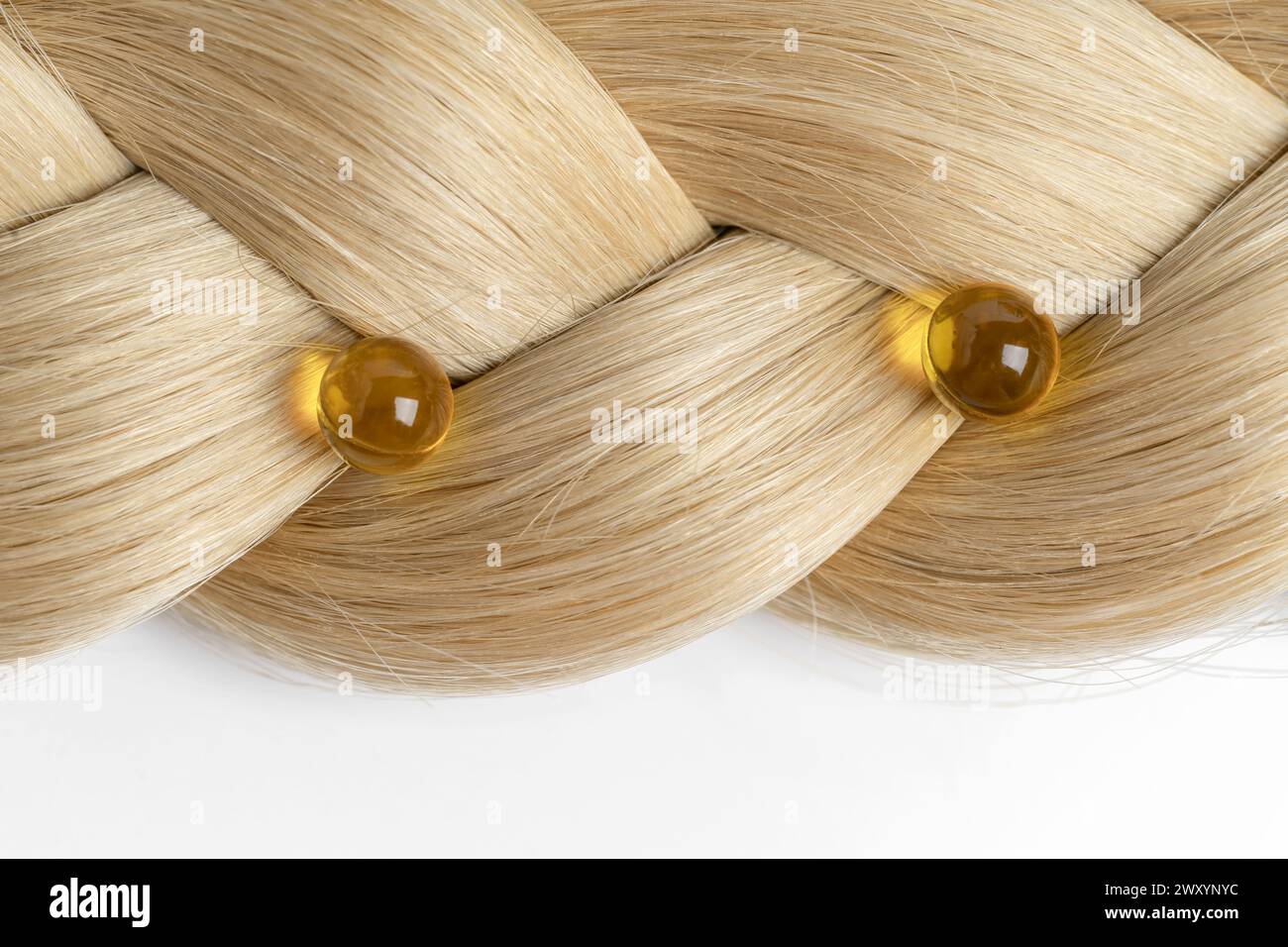 Eine Nahaufnahme eines wunderschön gewebten blonden Haarmusters mit zwei transluzenten, bernsteinfarbenen Ölkapseln, die strategisch platziert sind und einen luxuriösen hai zeigen Stockfoto