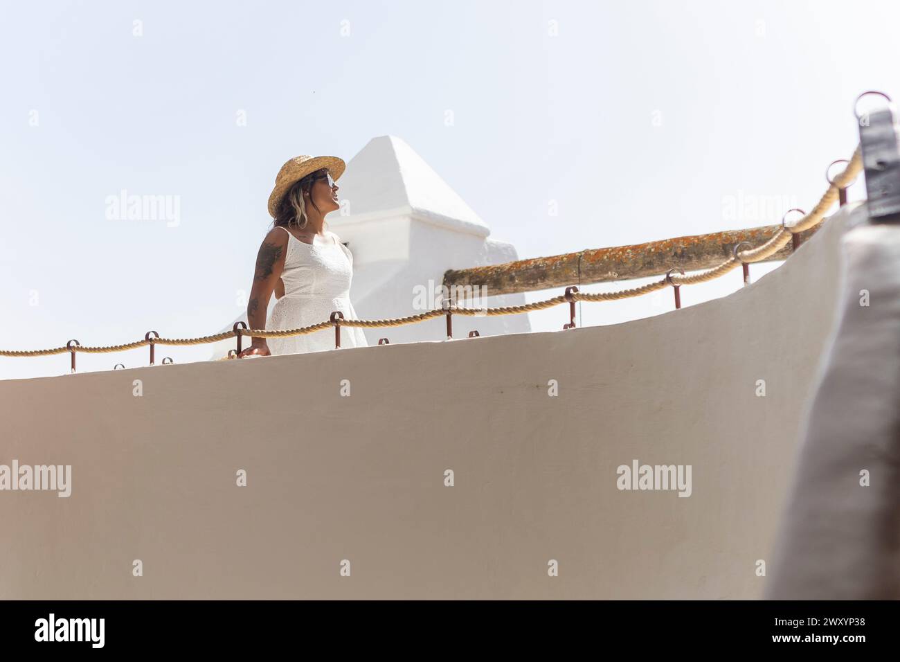 Eine Frau in weißem Kleid und Strohhut blickt von der Kamera weg und genießt einen ruhigen Moment auf ihrem Wochenendausflug. Stockfoto