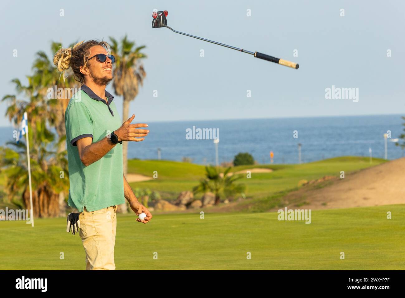 Ein junger Golfspieler mit Dreadlocks dreht seinen Golfschläger nach einem Schaukeln auf einem malerischen Golfplatz am Meer lässig um. Stockfoto