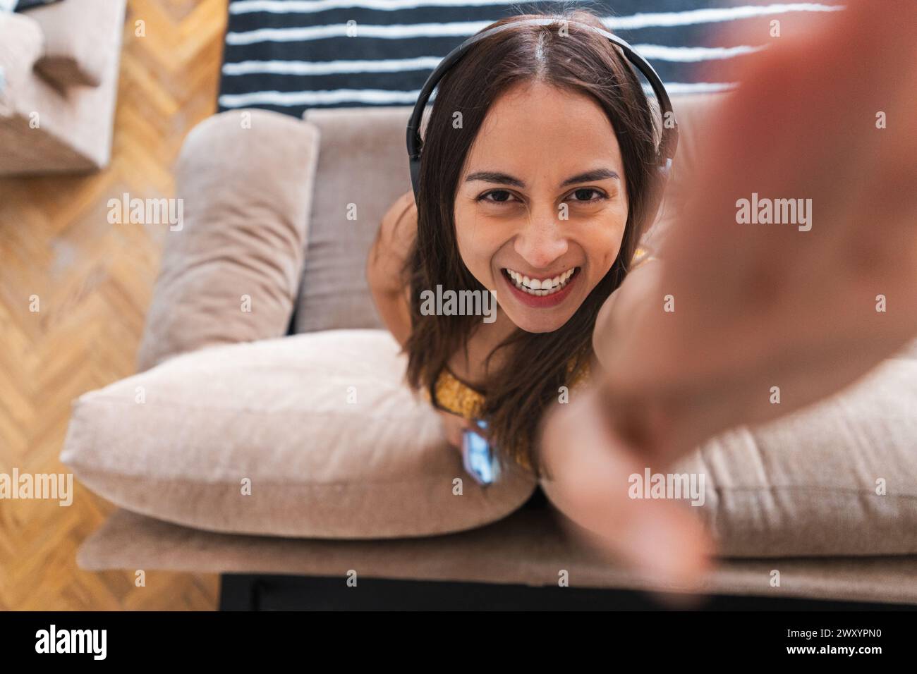 Eine fröhliche junge Frau mit Kopfhörern lächelt während eines Selfie in die Kamera und schafft so einen persönlichen und fesselnden Moment Stockfoto