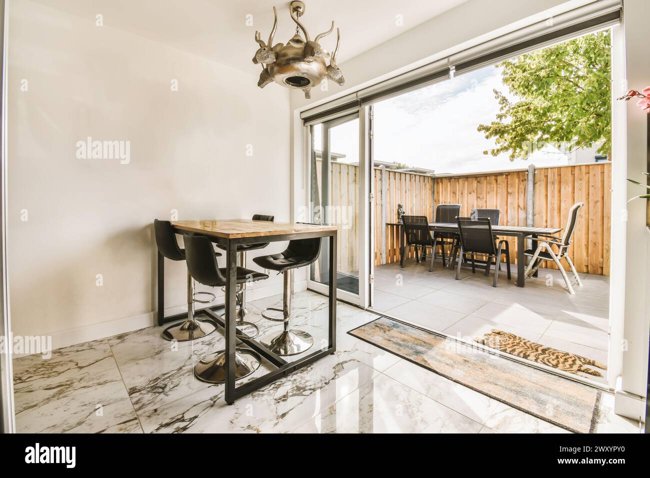 Heller Essbereich mit einem eleganten Tisch, der durch Glastüren zu einer einladenden Terrasse führt, die von einem einzigartigen Hirschkopf geschmückt ist. Stockfoto