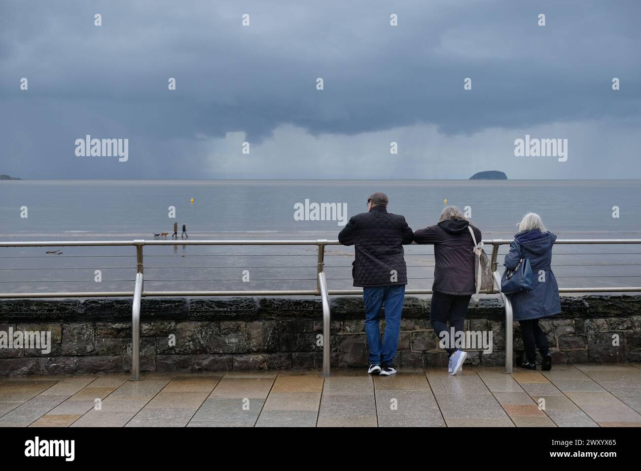 Dreier, Rentner, Leute, die auf einen grauen, nassen Strand blicken Stockfoto