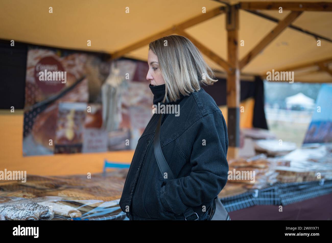 Junge Blondine wegen der Winterkälte auf der Stadtmesse mit handwerklichem Lebensmittelmarkt. Stockfoto