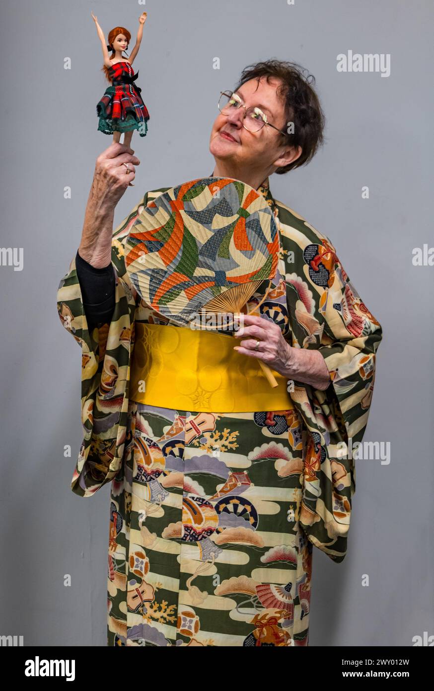 Central Library, Edinburgh, Schottland, Vereinigtes Königreich, 03. April 2024, die Ausstellung „Tanz um die Welt“ des Traditional Dance Forum of Scotland und des Edinburgh City Libraries for Granatapfeles Festival wird heute eröffnet und präsentiert Gegenstände aus über 20 Ländern. Im Bild: Die schottische Tanzkünstlerin und Historikerin Agnes Ness (81 Jahre), die die Ausstellung mitkuratierte, mit A Tartan Barbie Doll von Alison Harm of Psychomoda Sustainable Tartan. Quelle: Sally Anderson/Alamy Live News Stockfoto