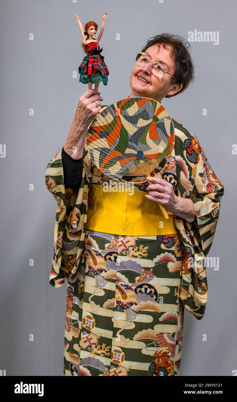 Central Library, Edinburgh, Schottland, Vereinigtes Königreich, 03. April 2024, die Ausstellung „Tanz um die Welt“ des Traditional Dance Forum of Scotland und des Edinburgh City Libraries for Granatapfeles Festival wird heute eröffnet und präsentiert Gegenstände aus über 20 Ländern. Im Bild: Die schottische Tanzkünstlerin und Historikerin Agnes Ness (81 Jahre), die die Ausstellung mitkuratierte, mit A Tartan Barbie Doll von Alison Harm of Psychomoda Sustainable Tartan. Quelle: Sally Anderson/Alamy Live News Stockfoto