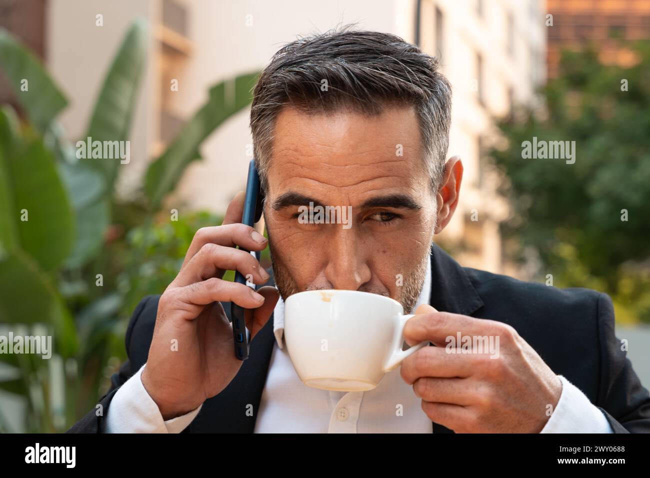 Porträt eines lächelnden Geschäftsmannes, der draußen mit einem Smartphone spricht. Stockfoto
