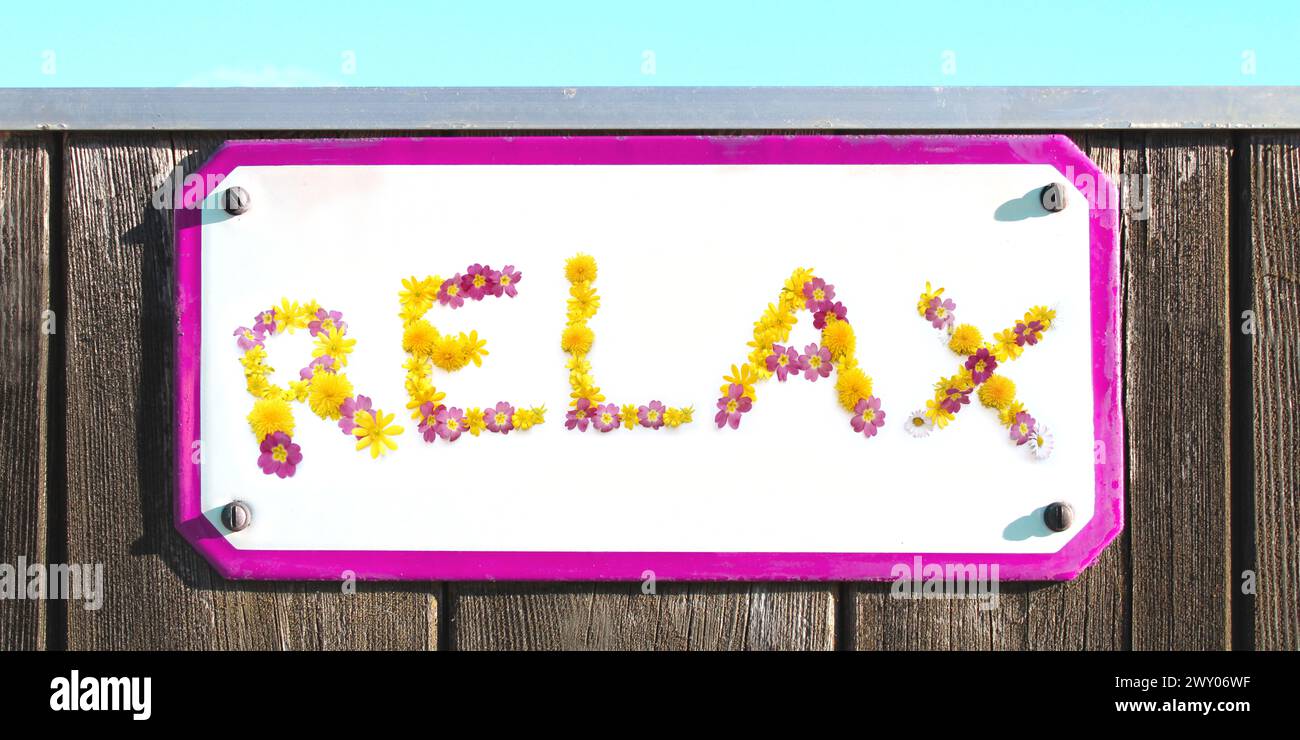 ENTSPANNEN SIE SICH von gelben, rosa Blumen Collage, Emaille, Metall, langgezogenen Steinkeramik Relax Schild an einer rustikalen Holzwand. Rosa Rahmen, türkisfarbener Himmel, sonnig Stockfoto