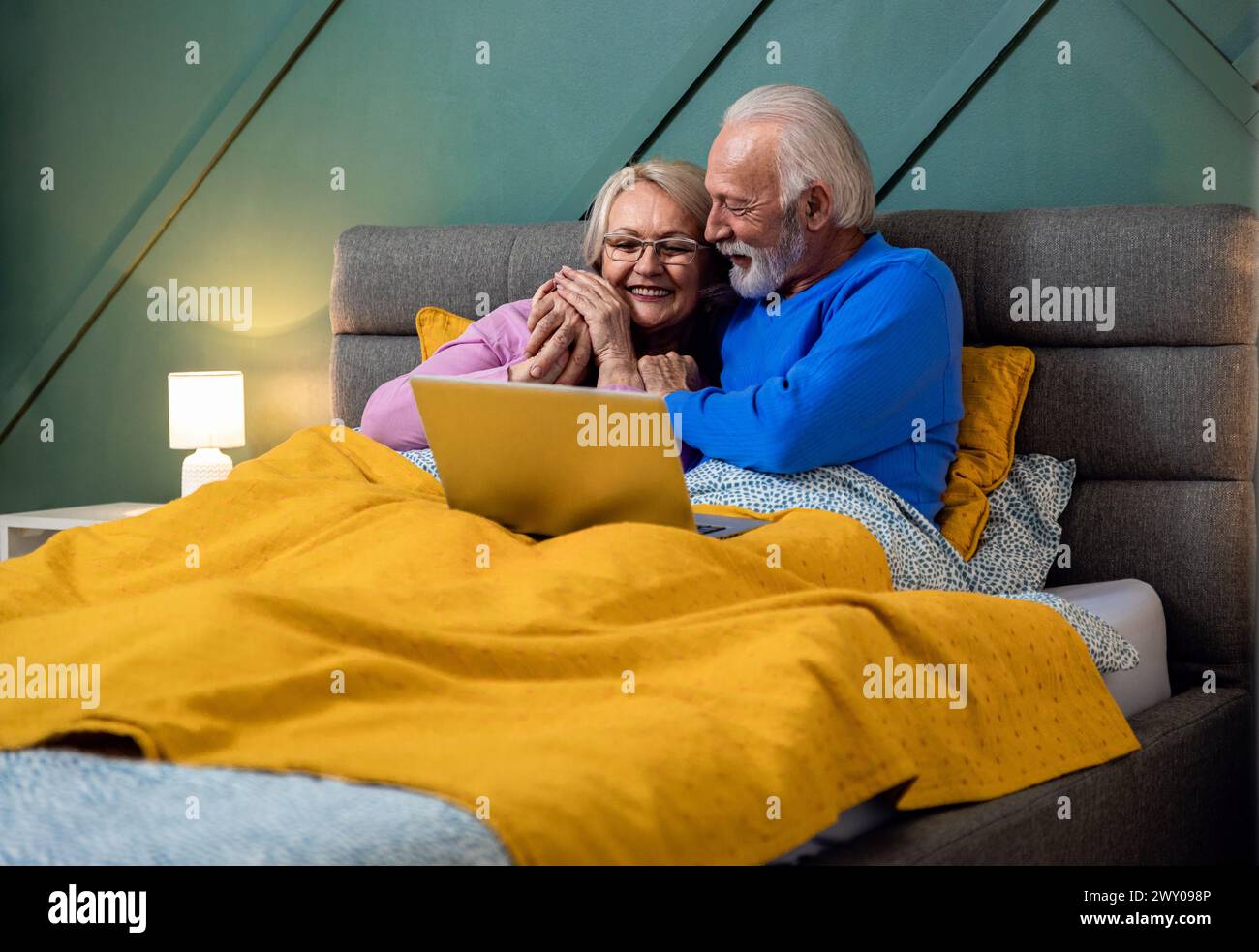 Lächelndes Seniorenpaar, das im Bett mit Laptop lag. Stockfoto