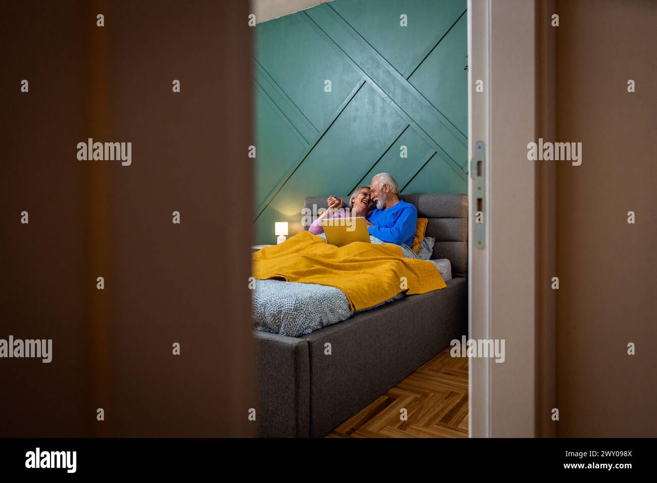 Lächelndes Seniorenpaar, das im Bett mit Laptop lag. Stockfoto