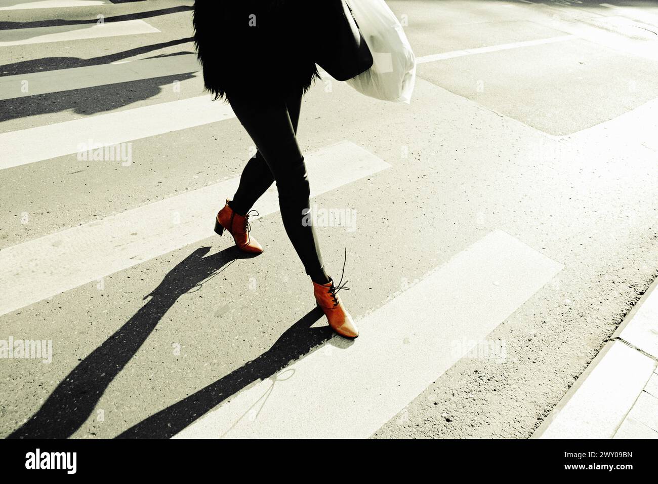 Straßenfotografie mit weiblichen Beinen, die auf der Straße des Crosswalk in die Innenstadt laufen. Stockfoto