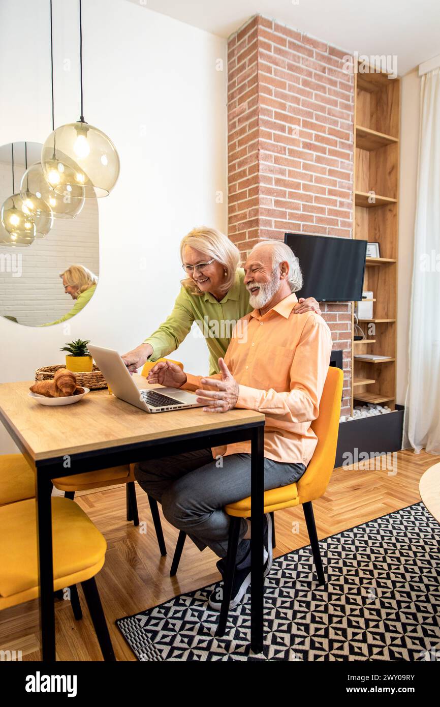 Lächelndes Seniorenpaar, das zu Hause im Wohnzimmer einen Laptop benutzt. Stockfoto
