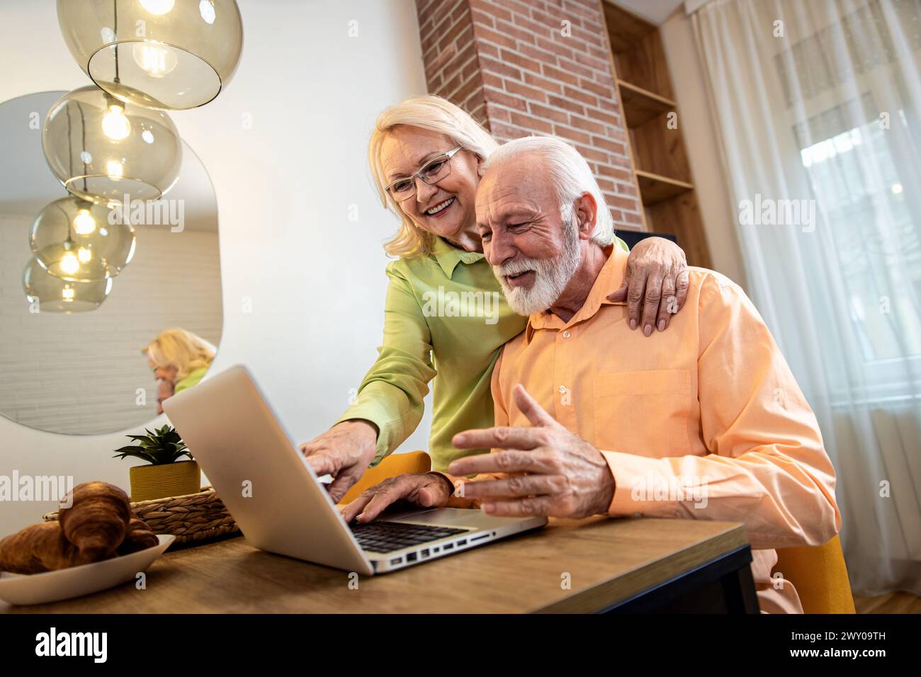 Lächelndes Seniorenpaar, das zu Hause im Wohnzimmer einen Laptop benutzt. Stockfoto