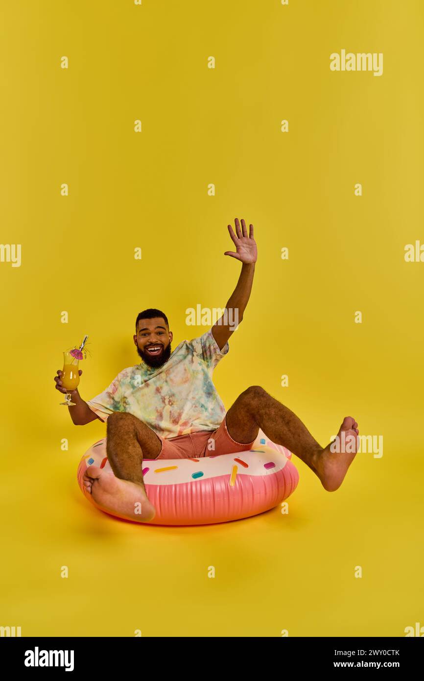 Ein Mann mit kontemplativem Ausdruck sitzt auf einem bunten aufblasbaren Objekt und schwimmt mühelos auf der Wasseroberfläche. Stockfoto