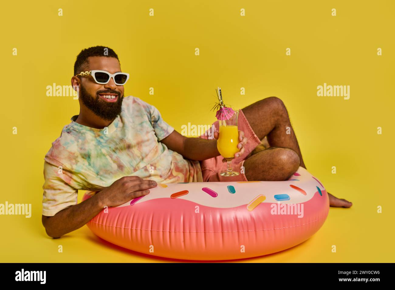 Ein Mann in entspannter Haltung sitzt auf dem pulsierenden rosa Donut-Schwimmer und strahlt ein Gefühl von Ruhe und Freizeit auf dem Wasser aus. Stockfoto