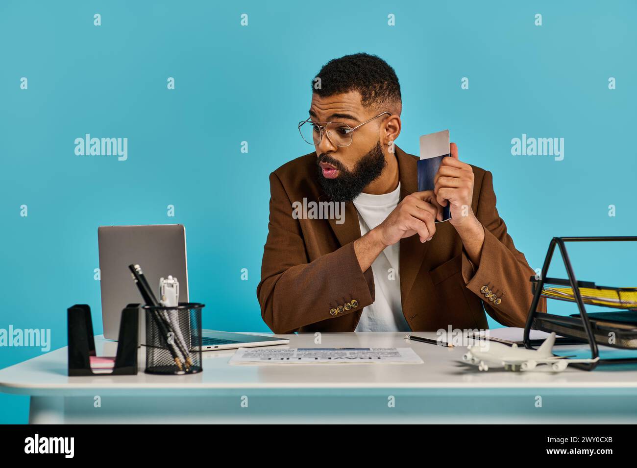 Ein fokussierter Mann, der tief in Gedanken an einem Schreibtisch sitzt, eine Kreditkarte in der Hand hält und über einen Kauf oder eine finanzielle Entscheidung nachdenkt. Stockfoto