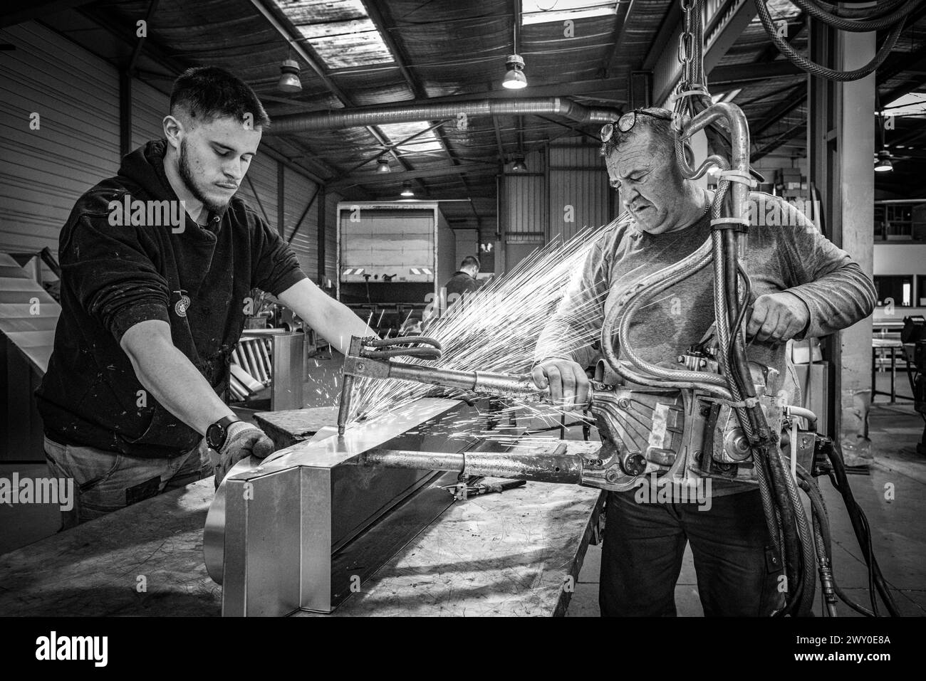 Zwei Arbeiter, ein junger und ein Senior, führen Punktschweißungen von Stahlblechen in einer Fertigungswerkstatt durch. Stockfoto