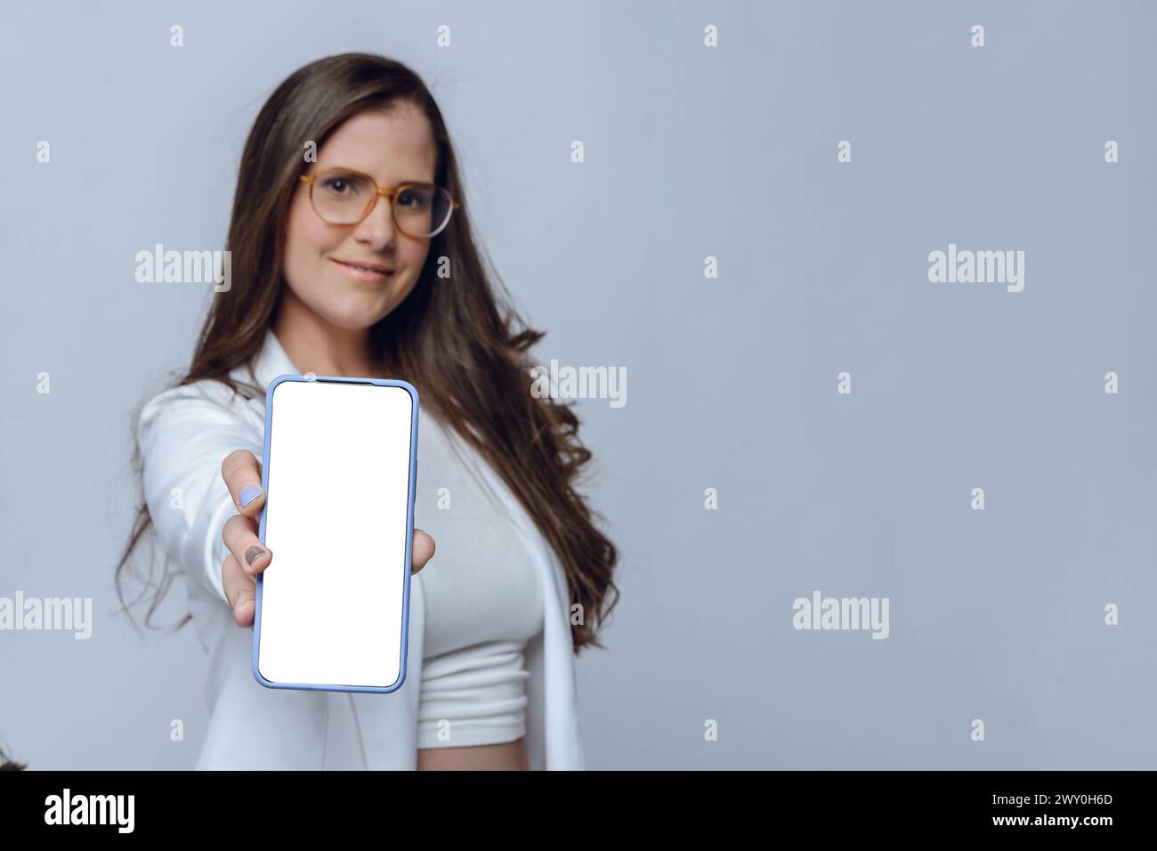 Altina junge Frau lächelt unscharf mit ausgestreckter Hand, zeigt mit ihrer Hand weißen Bildschirm des Telefons, Fokus auf Telefon, Studio-Aufnahme mit weißem Hintergrund Stockfoto