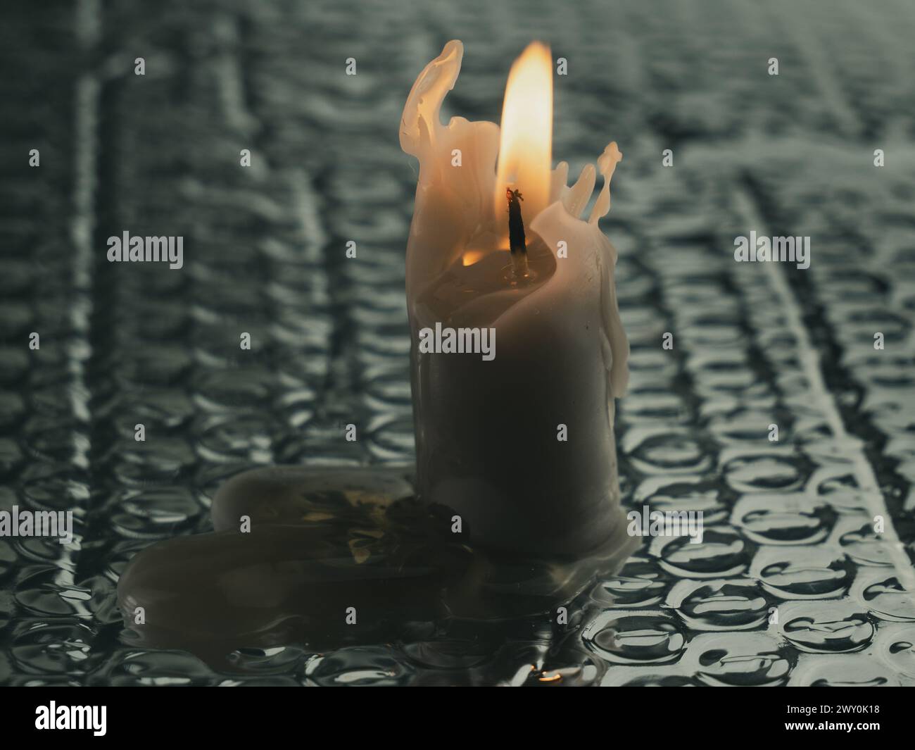 Eine weiße Kerze auf dem Boden mit Wassertropfen Stockfoto
