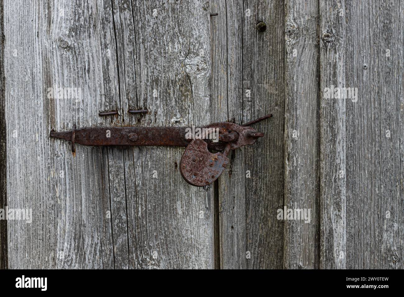 Nahaufnahme des alten rostigen Vorhängeschlosses auf einer alten grauen Holztür. Stockfoto