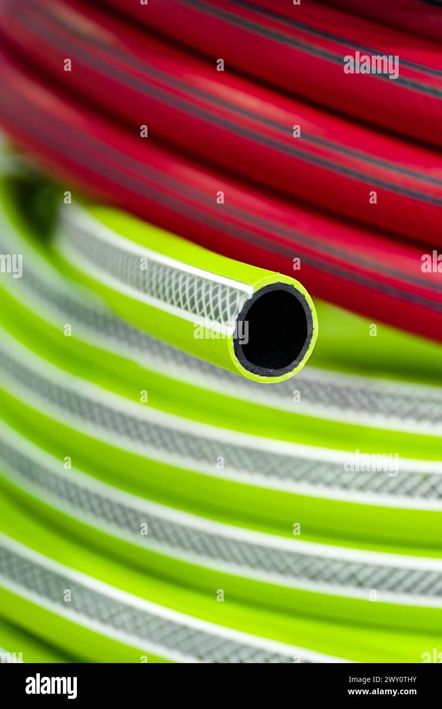 Zusammengerollter bunter Gartenschlauch, rot und grün, Nahaufnahme, selektiver Fokus, abstrakter Gartenhintergrund Stockfoto