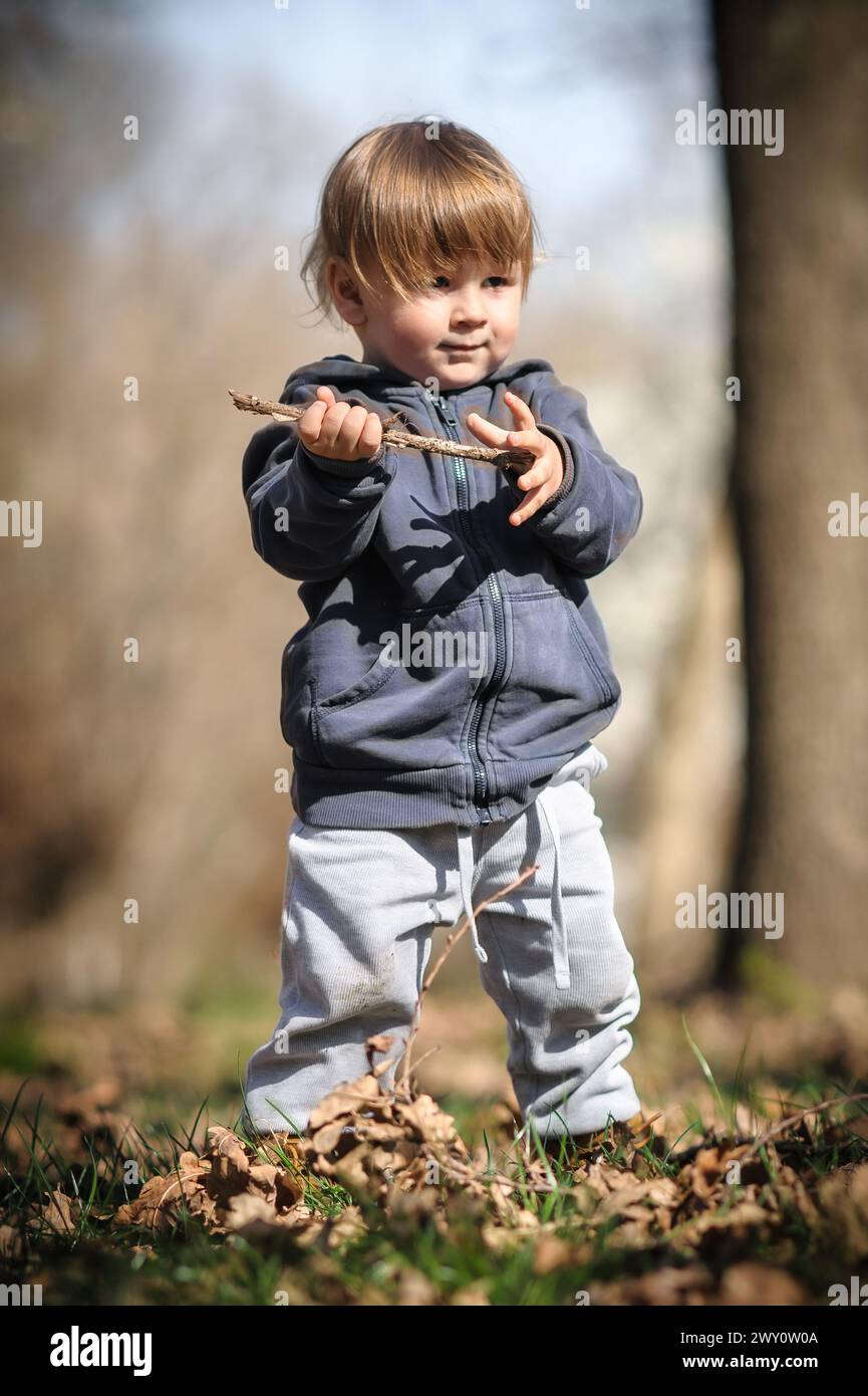 Herbstabenteuer für Kleinkinder. Kurioses Kind hockt sich zwischen gefallenen Blättern und entdeckt die Wunder der Natur. Kinder spielen im Freien Stockfoto