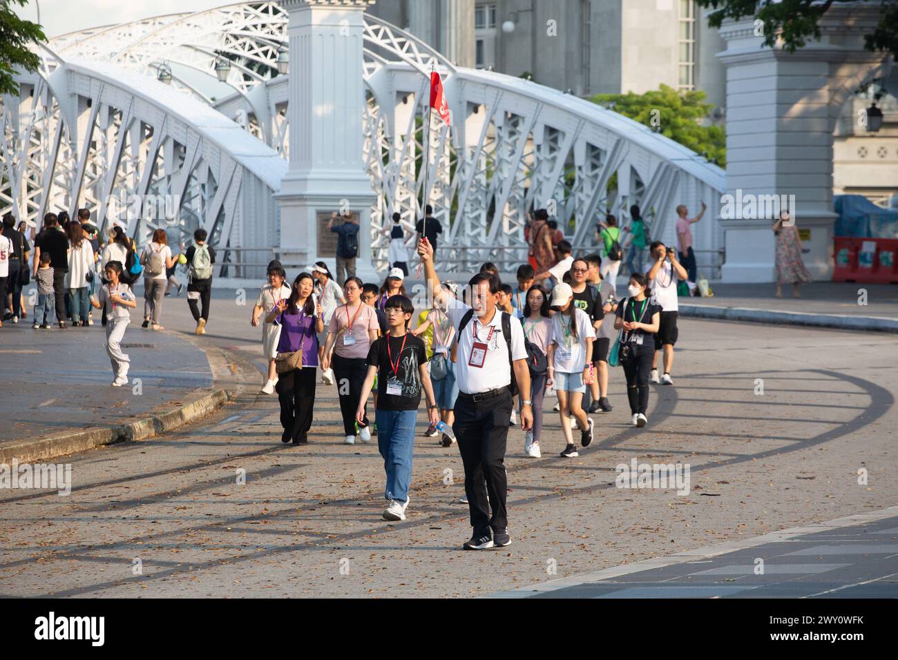 Ein männlicher chinesischer lizenzierter Reiseleiter hält eine Stangenfahne, um sicherzustellen, dass seine Gruppe ihm in der Mitte der Straße zum nächsten Ziel folgt. Singapur. Stockfoto
