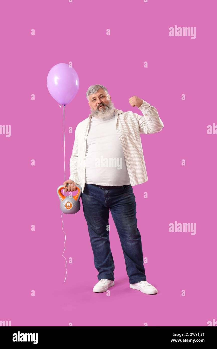 Seniorenmann mit Ballon und Kettlebell, der Muskeln auf rosa Hintergrund zeigt Stockfoto