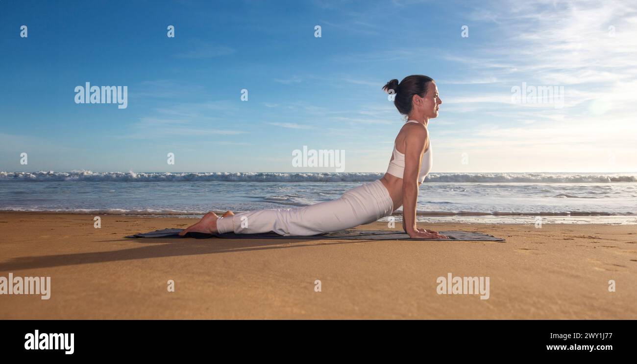 Yoga im Freien am Strand, Frau in aufwärts gerichteter Hundespitze an einem Sandstrand in der Sonne Stockfoto