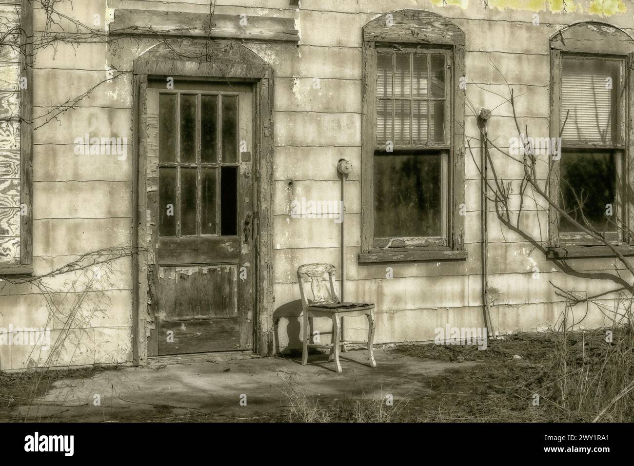 Nahaufnahme eines alten verlassenen Gebäudes, in dem ein Holzstuhl neben der Tür mit kaputten Fensterscheiben sitzt Stockfoto