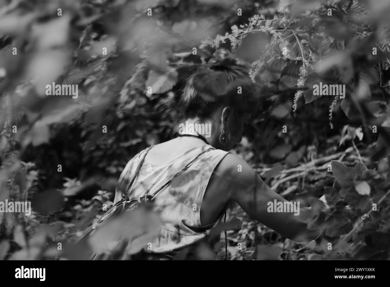 In den Tiefen der Umarmung der Natur steht eine Abenteurerin hoch, ihre Figur in dickem Laub gehüllt, in einem zeitlosen Schwarz-weiß-Schuss gefangen. Stockfoto