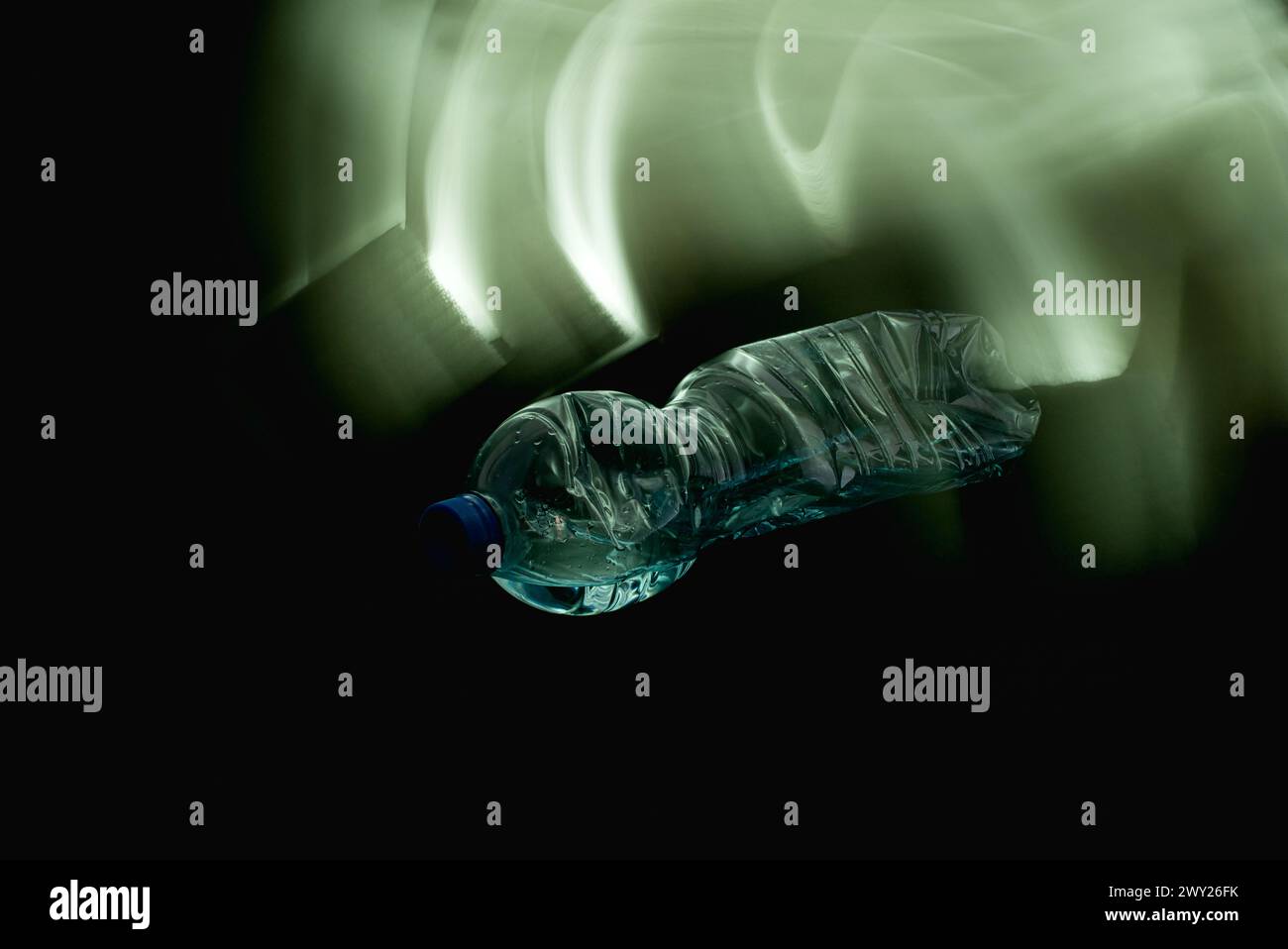 Eine zerquetschte Kunststoffflasche, die teilweise mit Wasser gefüllt war, horizontal auf schwarzem Hintergrund in einem 45-Grad-Winkel mit dem Schraubverschluss in Richtung des kam Stockfoto